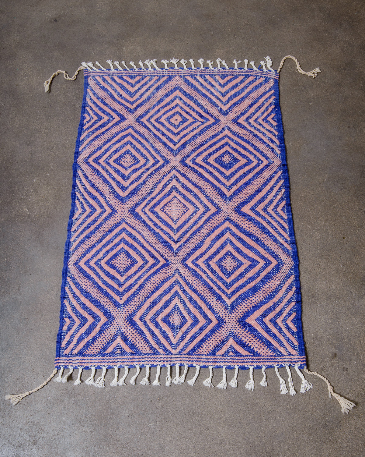 Small Kelim Rug in blue and pink laying on concrete studio floor.